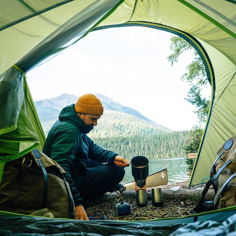 Man cooking in green tent with mountains visible in tent door