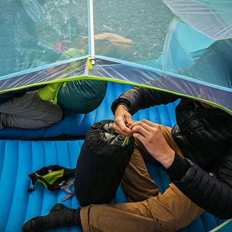 Man opening sleeping bag pack while sitting on pad