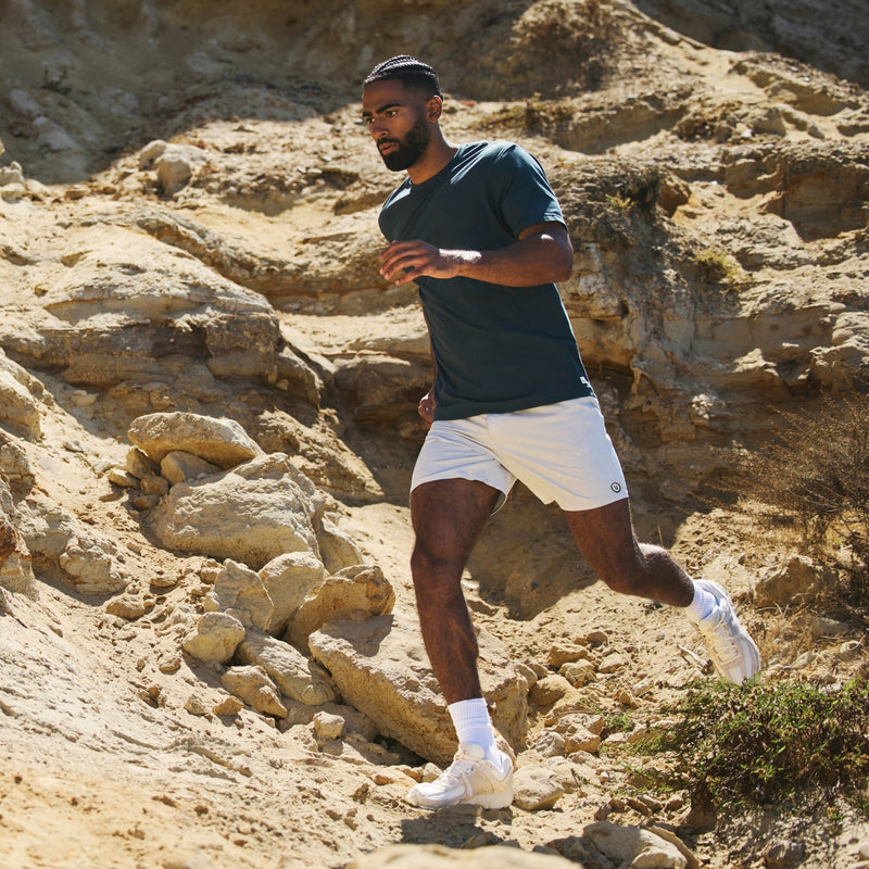 Man running in rocky environment. Blue short sleeve and white running shorts.