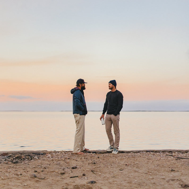 Two men standing on beach with sun setting
