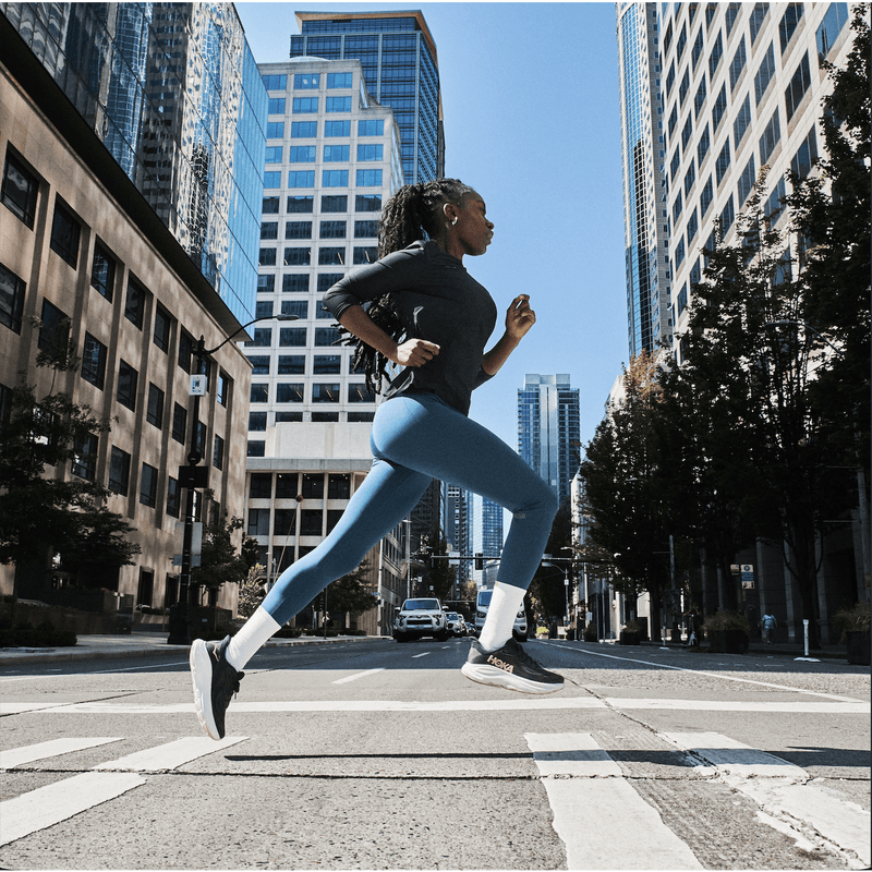Woman running down street with black running shoes on with white soles