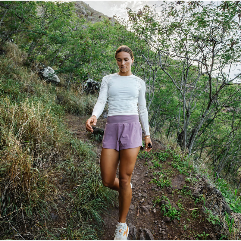 Women walking down grassy hill with white long sleeve and purple shorts