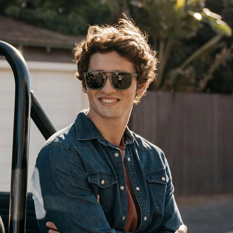 Man smiling with black sunglasses on. Leaning against car with arms crossed